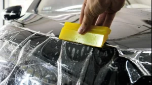 Installer squeegeeing paint protection film onto a black car bonnet, PPF vs ceramic coating in Dubai